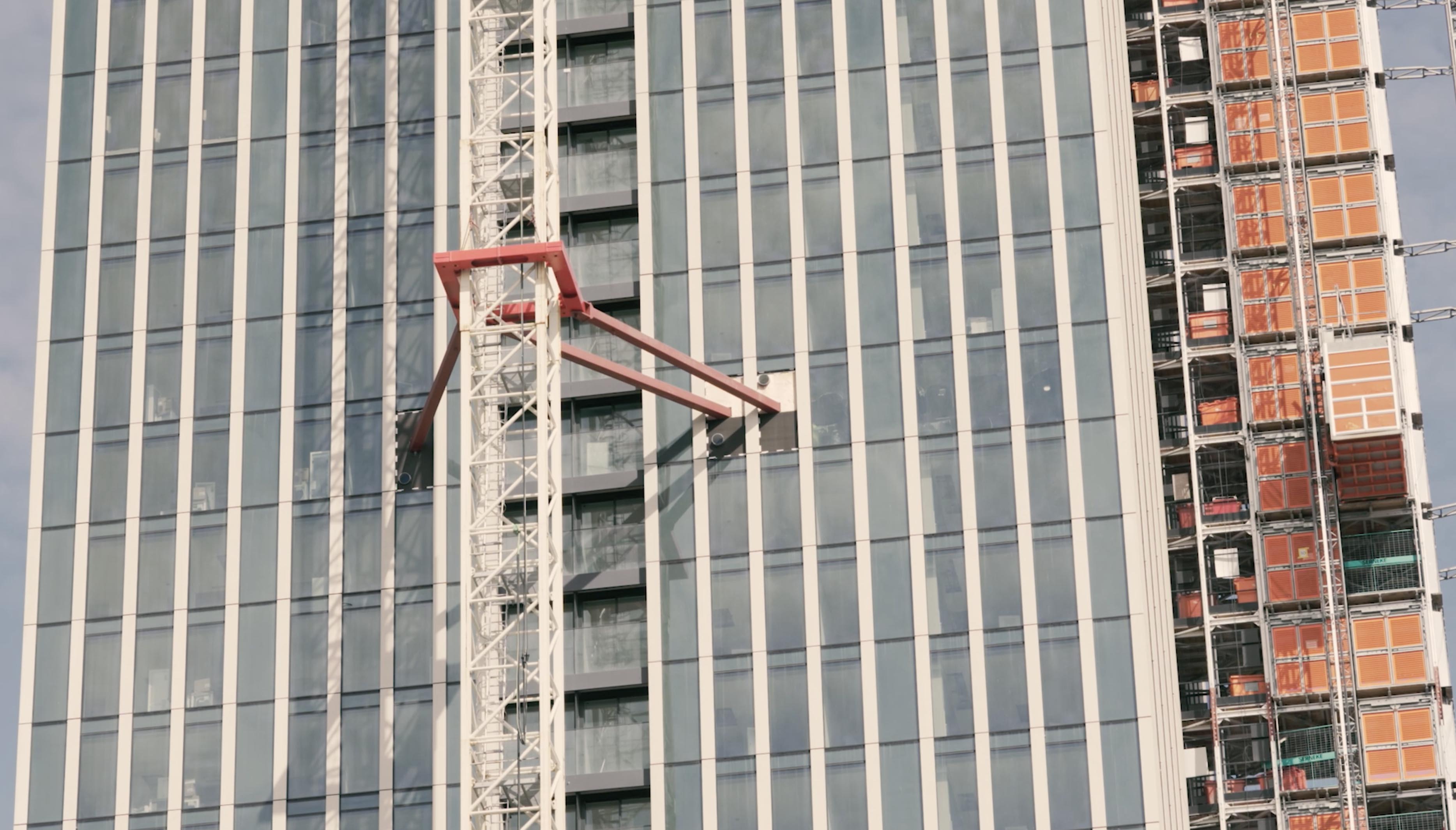 A crane is fixed to the facade of a skyscraper, using steel beams.