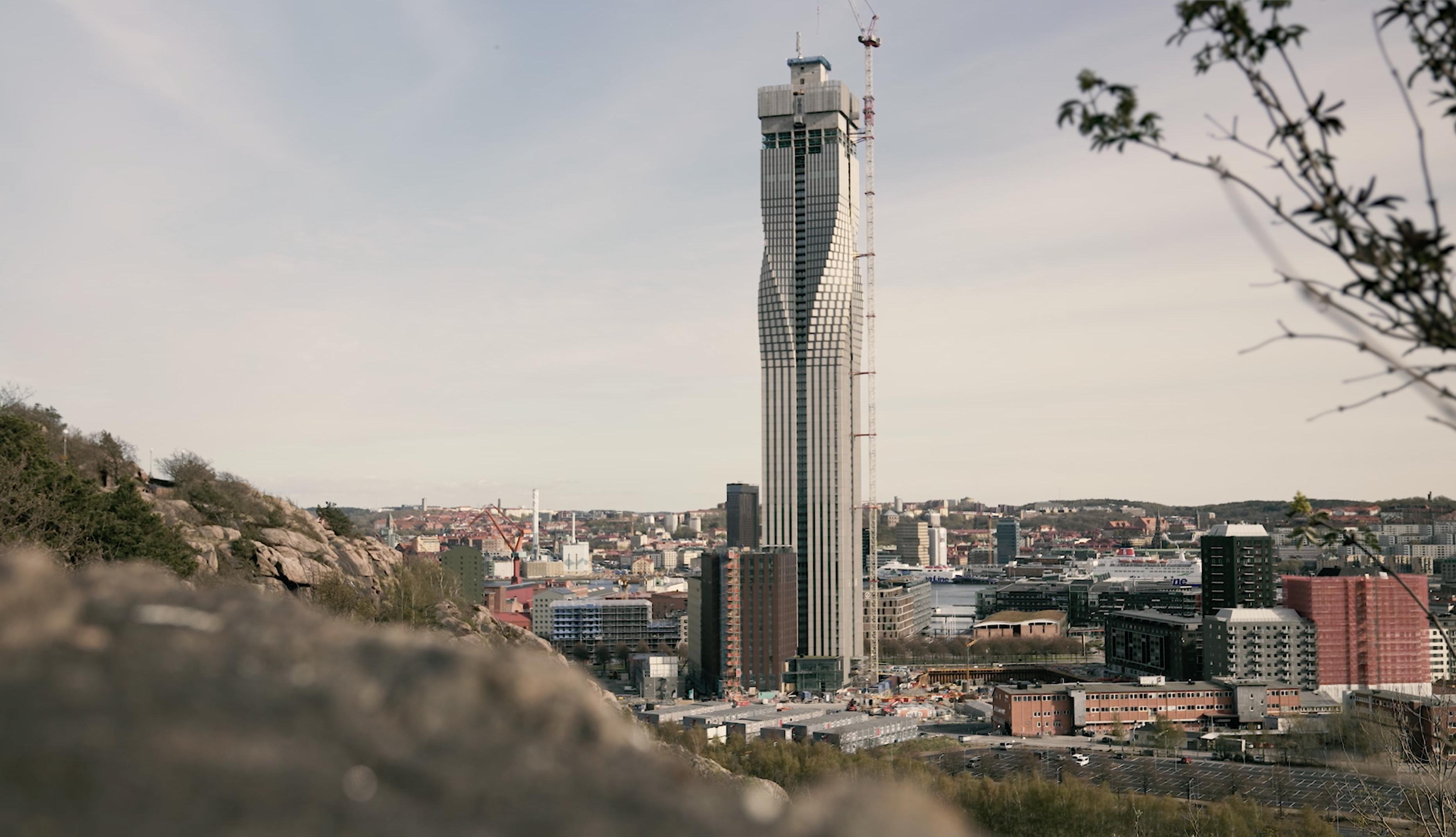 City skyline in the background, with a tower as the tallest building. The outline of a cliff in the foreground.