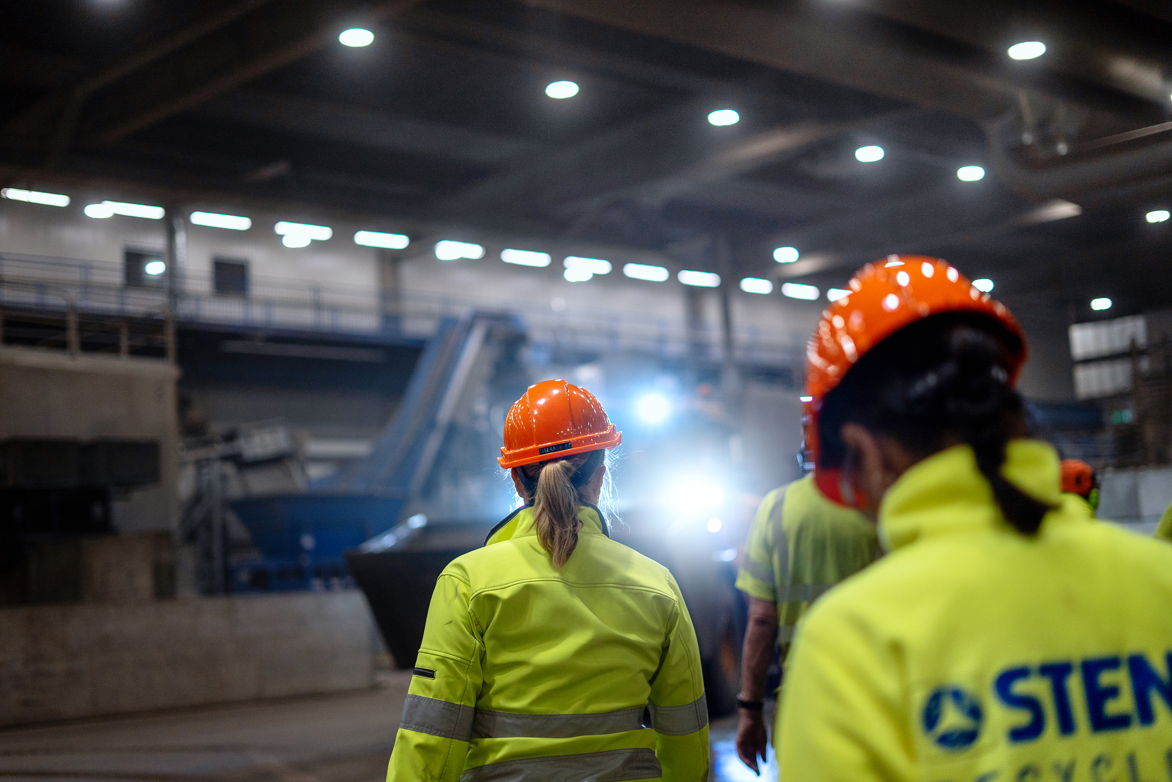 A group of Stena Metall Group employees in hi-vis protective gear walk together in a Stena facility.