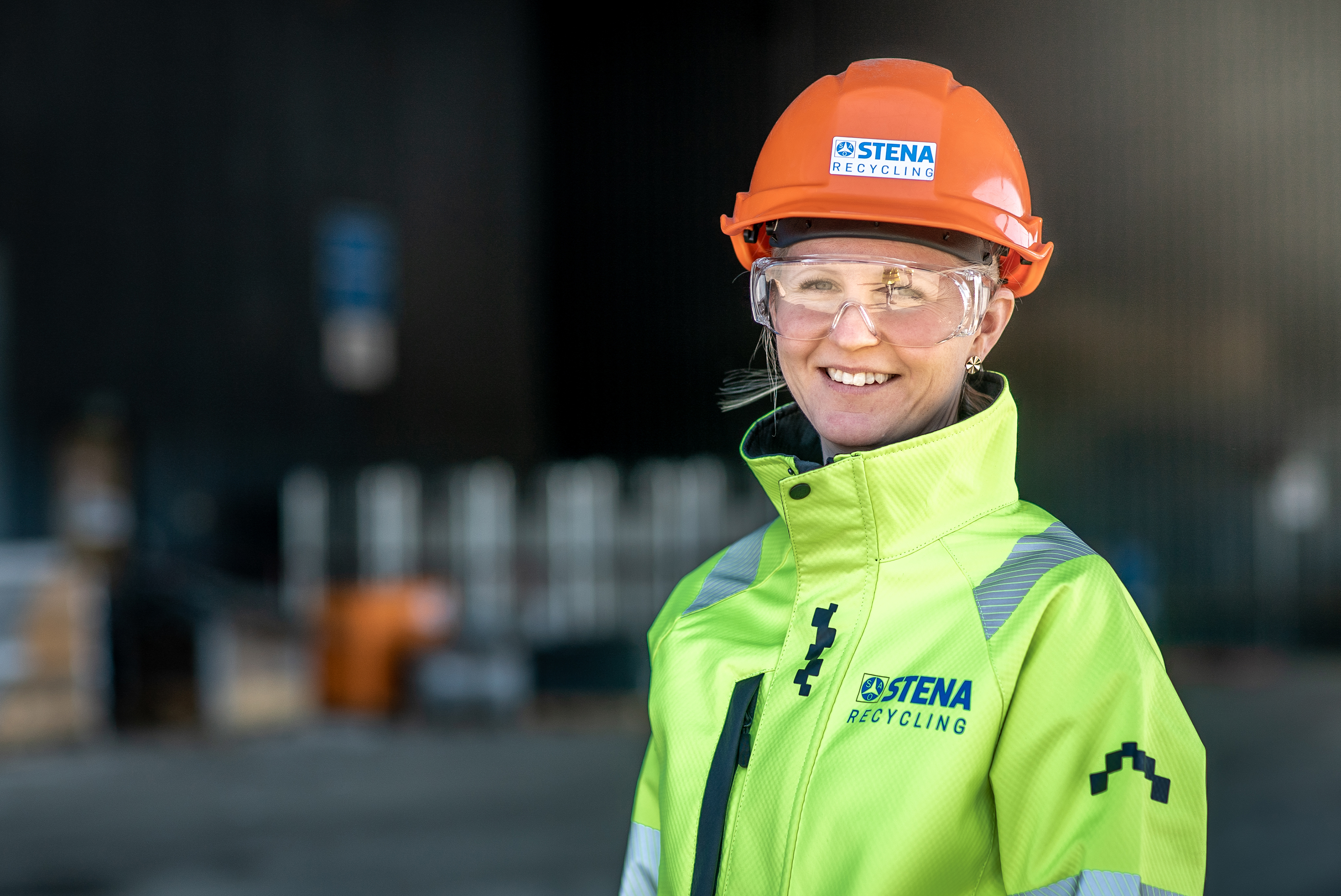 Female Stena Metall Group expert looking into the camera, dressed in a reflective work jacket and hardhat with Stena Recycling logo