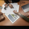 Three Stena Metall Group employees’ hands rest on a desk with plans, a laptop and a small jar of recycled material.