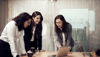 Three female employees at Stena Circular Consulting stand around a table, looking and pointing at a laptop which stands on the table.