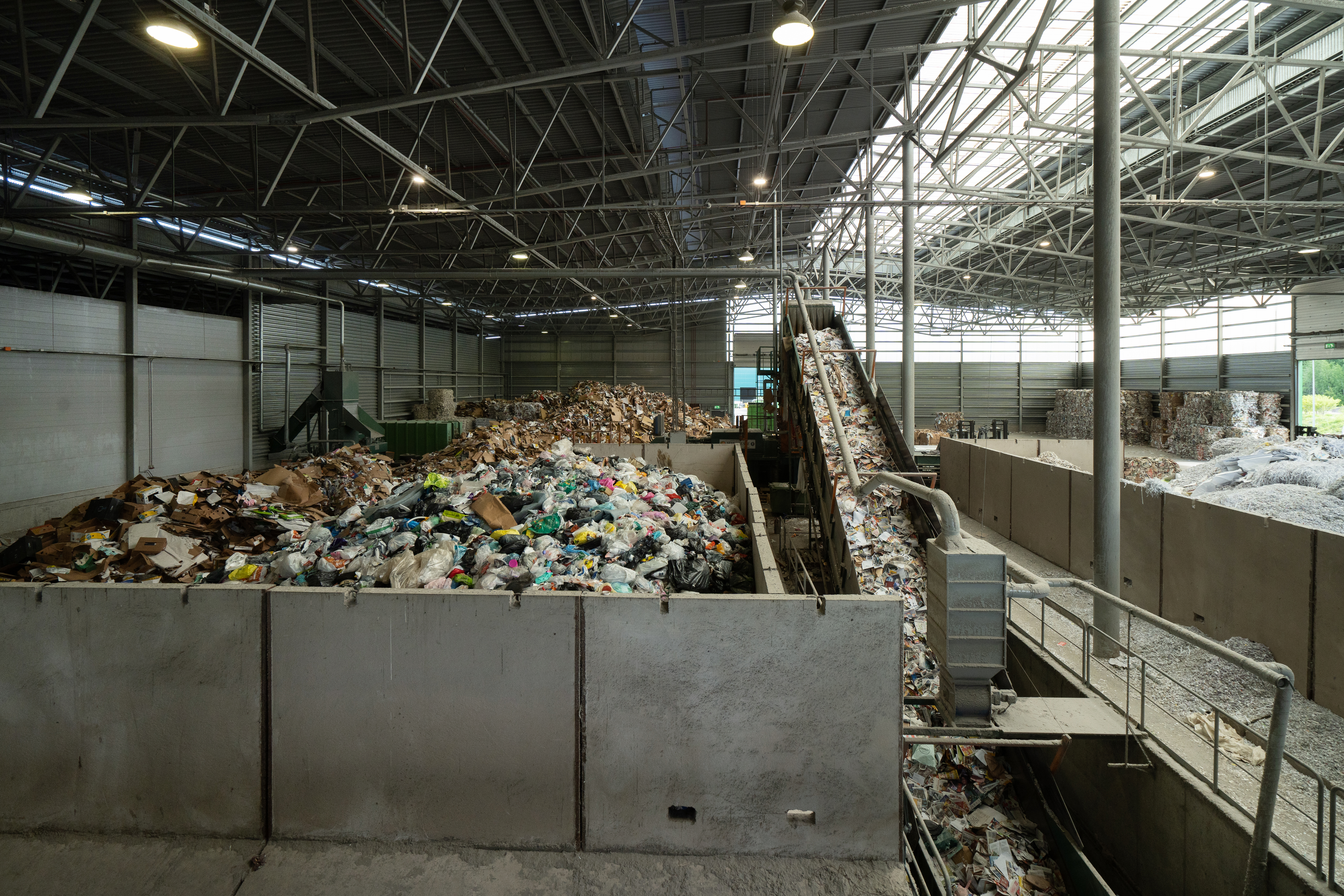The interior of a recycling facility, with containers and conveyor belts filled with plastic and paper waste.