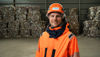 Close-up of a male Stena Recycling employee in hi-vis protective gear, standing in front of a piles with packaged paper waste