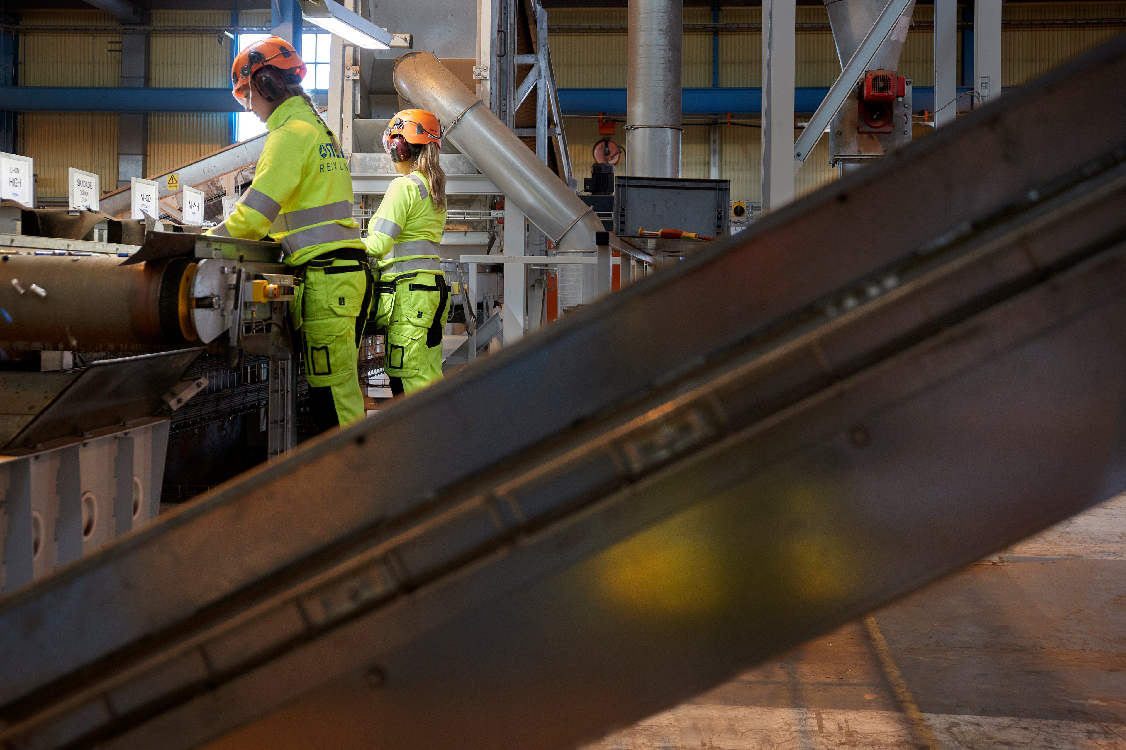 Two female Stena Metall Group employees in hi-vis protective gear at  work in a Stena Recycling facility.